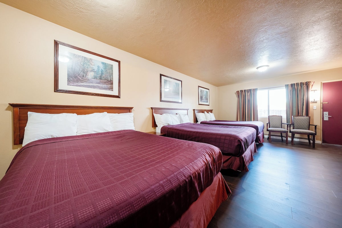 A hotel room with three beds, a chair, and framed pictures on the wall.