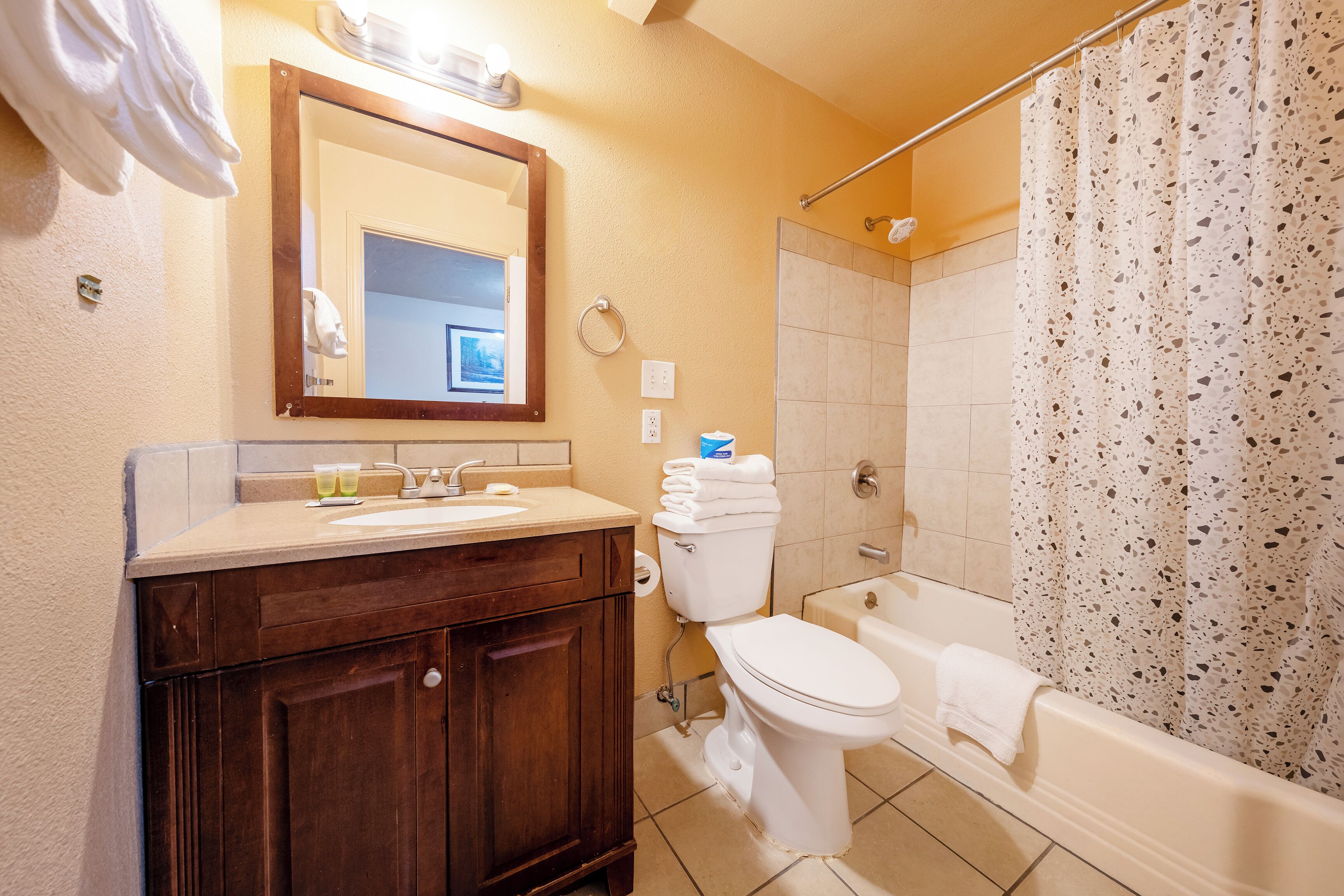 A bathroom with a wooden vanity, a toilet, a bathtub, and a shower curtain.