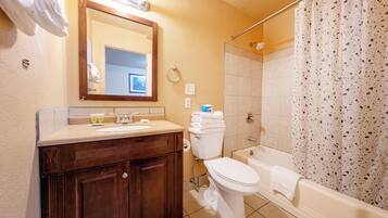 A bathroom with a wooden vanity, a toilet, a bathtub, and a shower curtain.