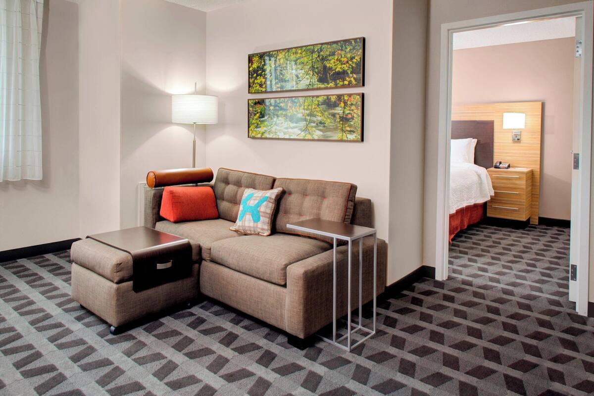 A hotel room with a sofa, a small table, a lamp, and a bed with a nightstand.