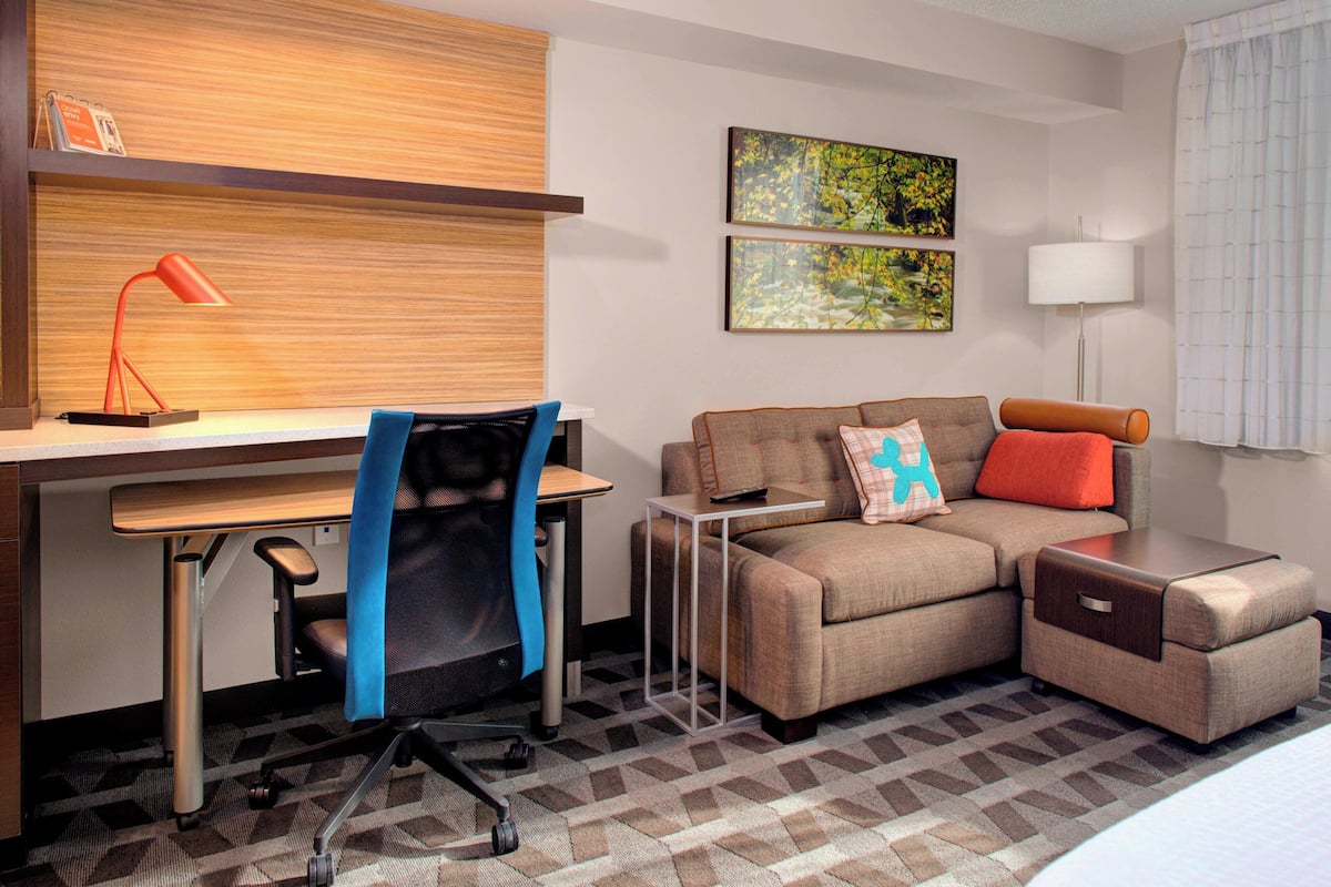 A hotel room with a desk, office chair, sofa, and ottoman.
