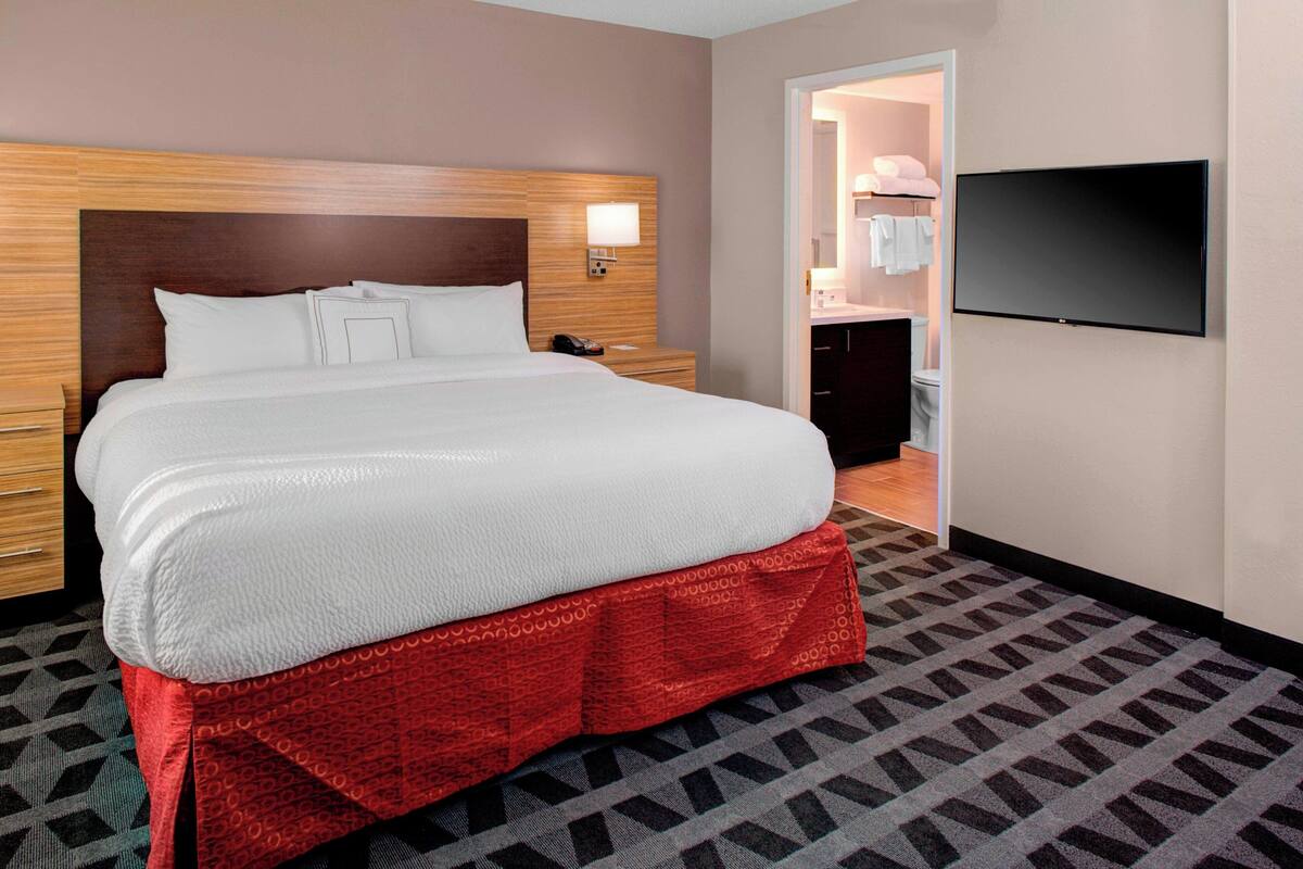 A hotel room with a large bed, a TV mounted on the wall, and a bathroom visible through an open door.