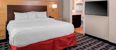 A hotel room with a large bed, a TV mounted on the wall, and a bathroom visible through an open door.