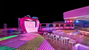 Área externa bem iluminada com palco, assentos e um bar.