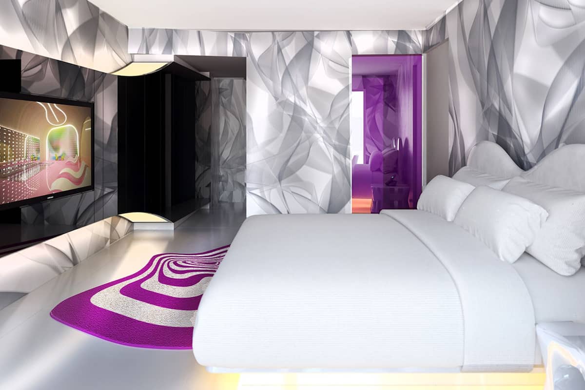 A modern bedroom with a large bed, a TV, and a unique geometric wall design.