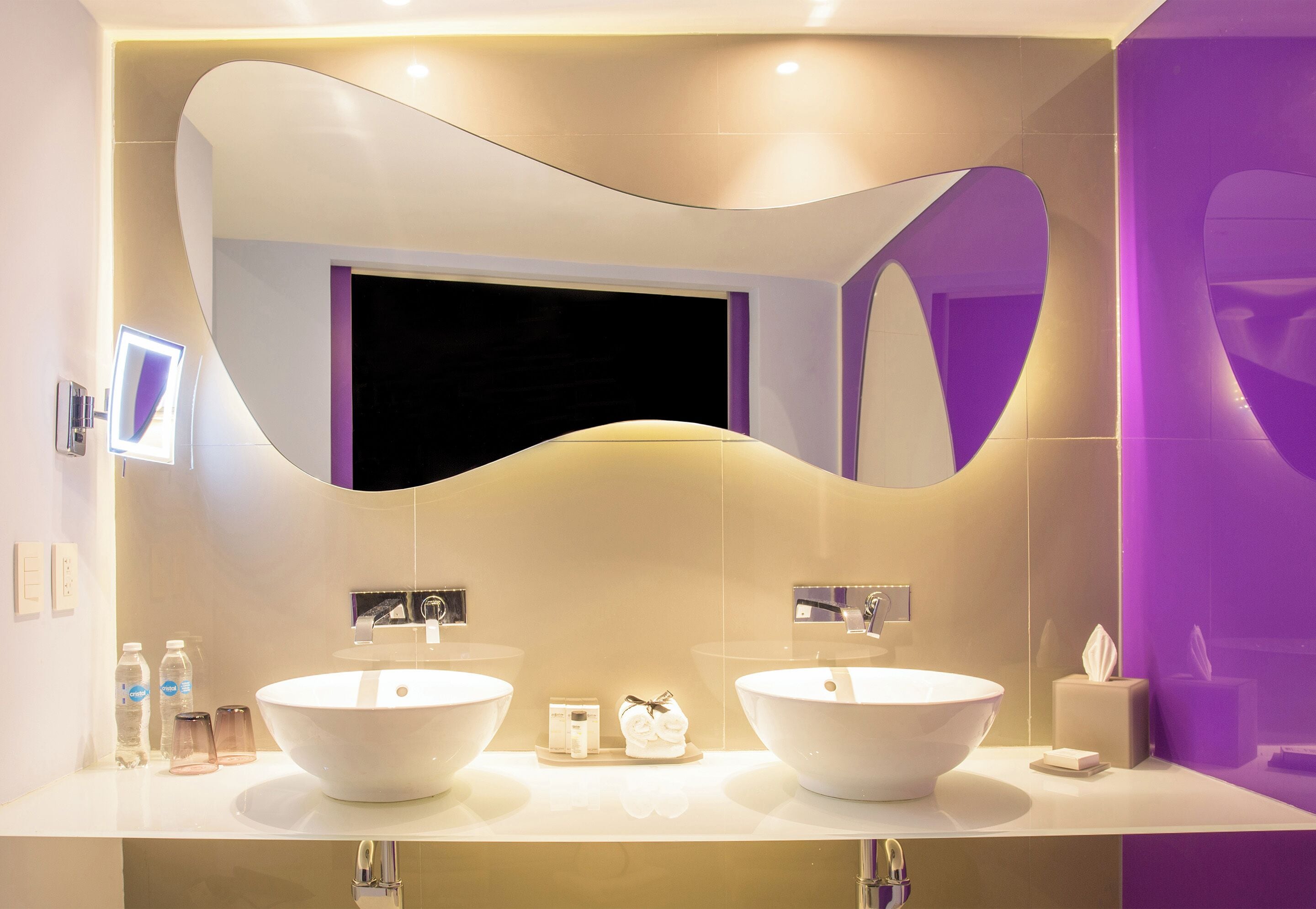 A modern bathroom with two sinks, a large mirror, and a purple accent wall.