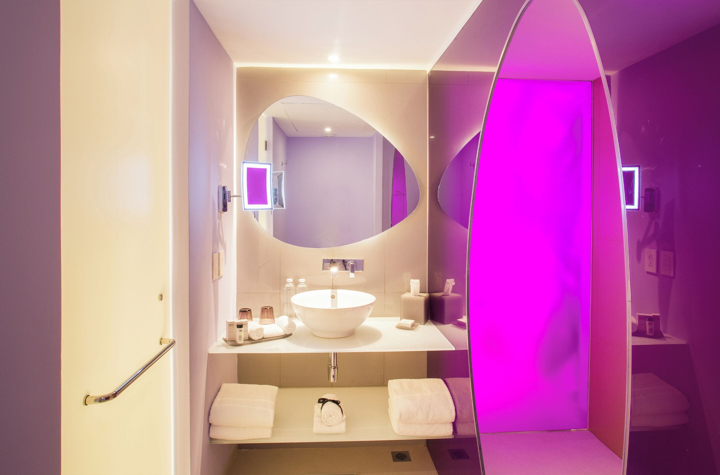 Un baño moderno con un espejo ovalado grande, un lavamanos blanco y un mueble de tocador con dos barras para toallas.