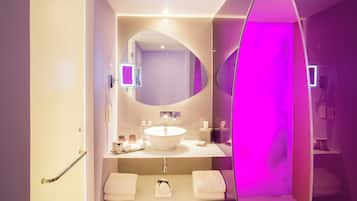 Un baño moderno con un espejo ovalado grande, un lavamanos blanco y un mueble de tocador con dos barras para toallas.