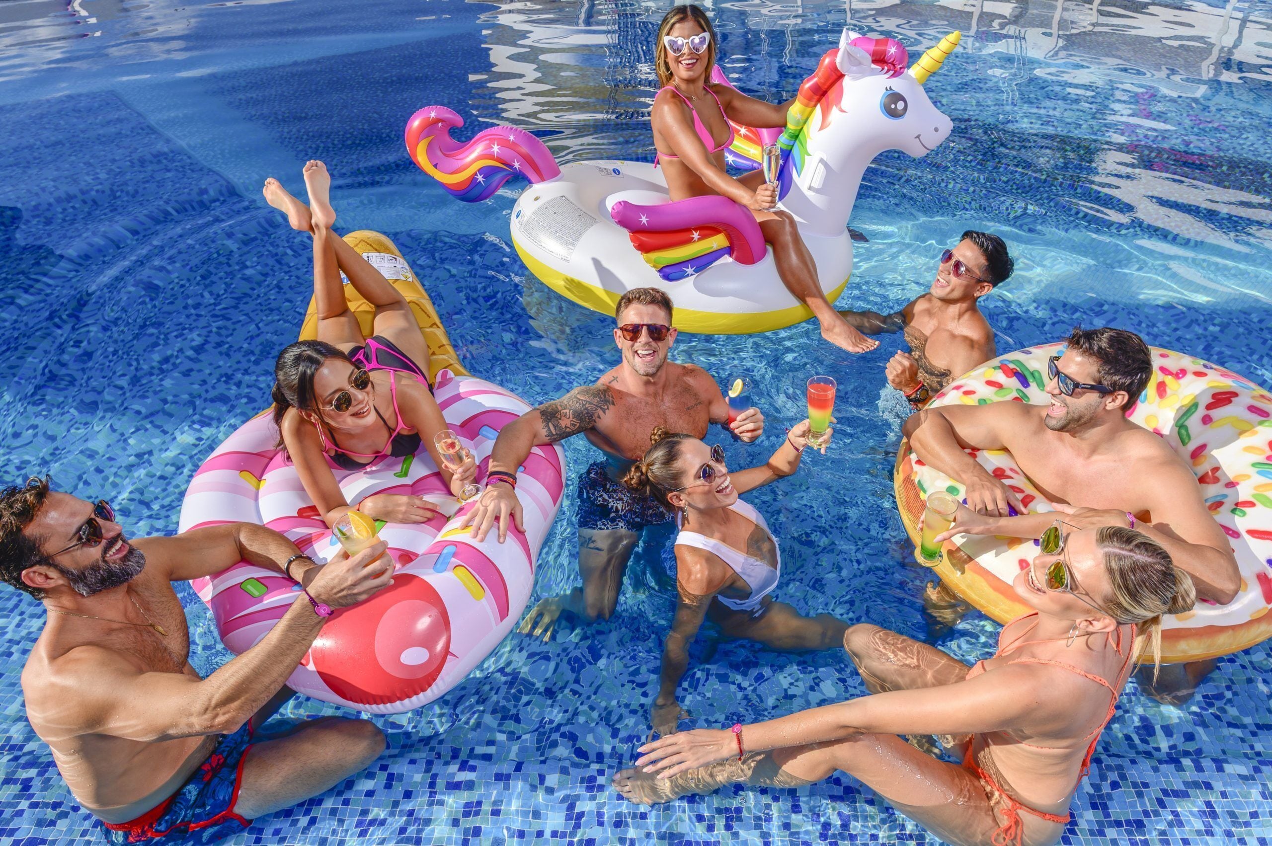 A group of people in a swimming pool with inflatable unicorn floats.