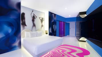 Une chambre d’hôtel moderne avec un grand lit, un tapis rose vif et des œuvres d’art abstraites accrochées au mur.