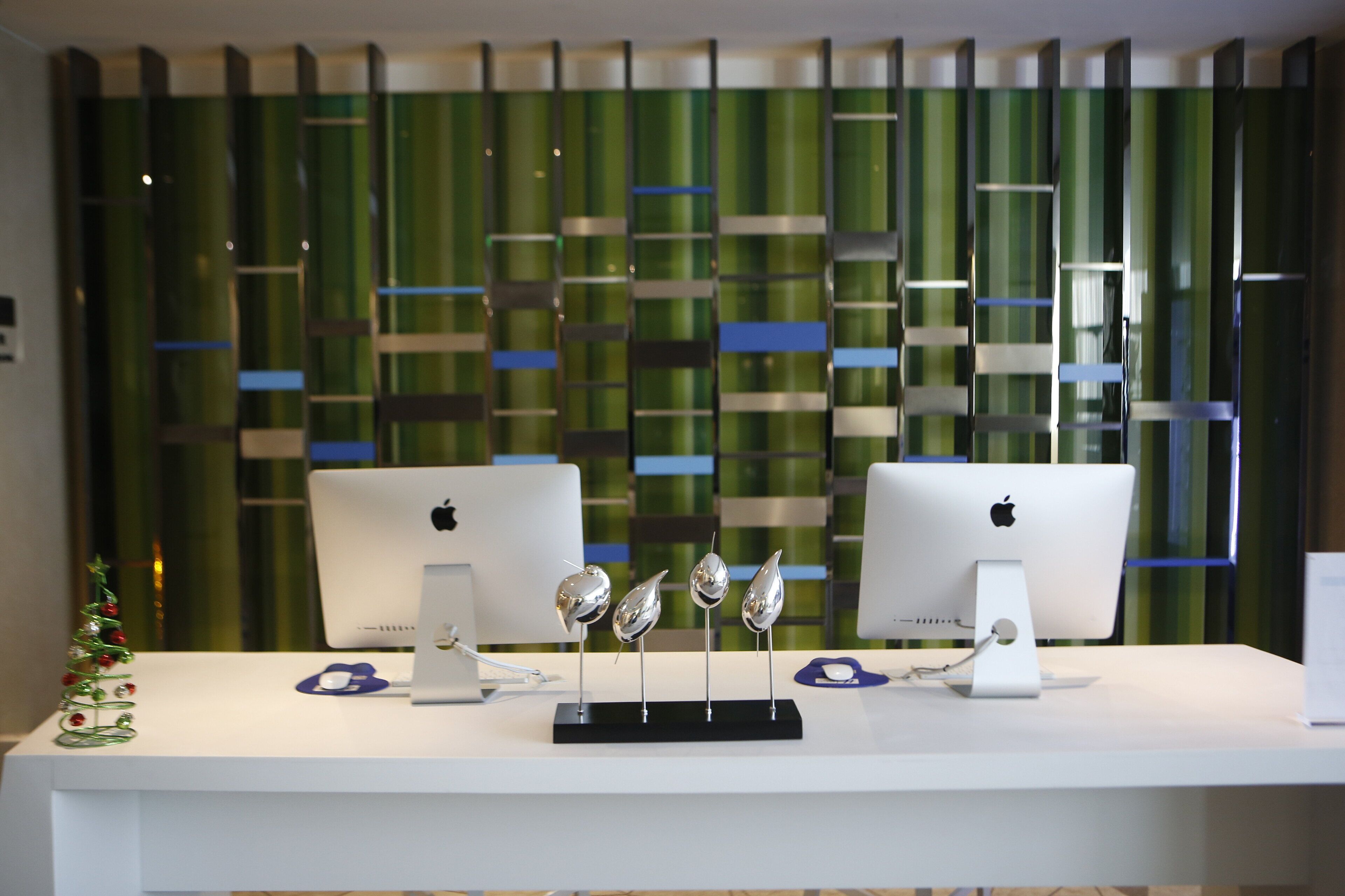 Deux ordinateurs Apple iMac sont posés sur un bureau blanc, et un présentoir décoratif soutient quatre cuillères en argent.