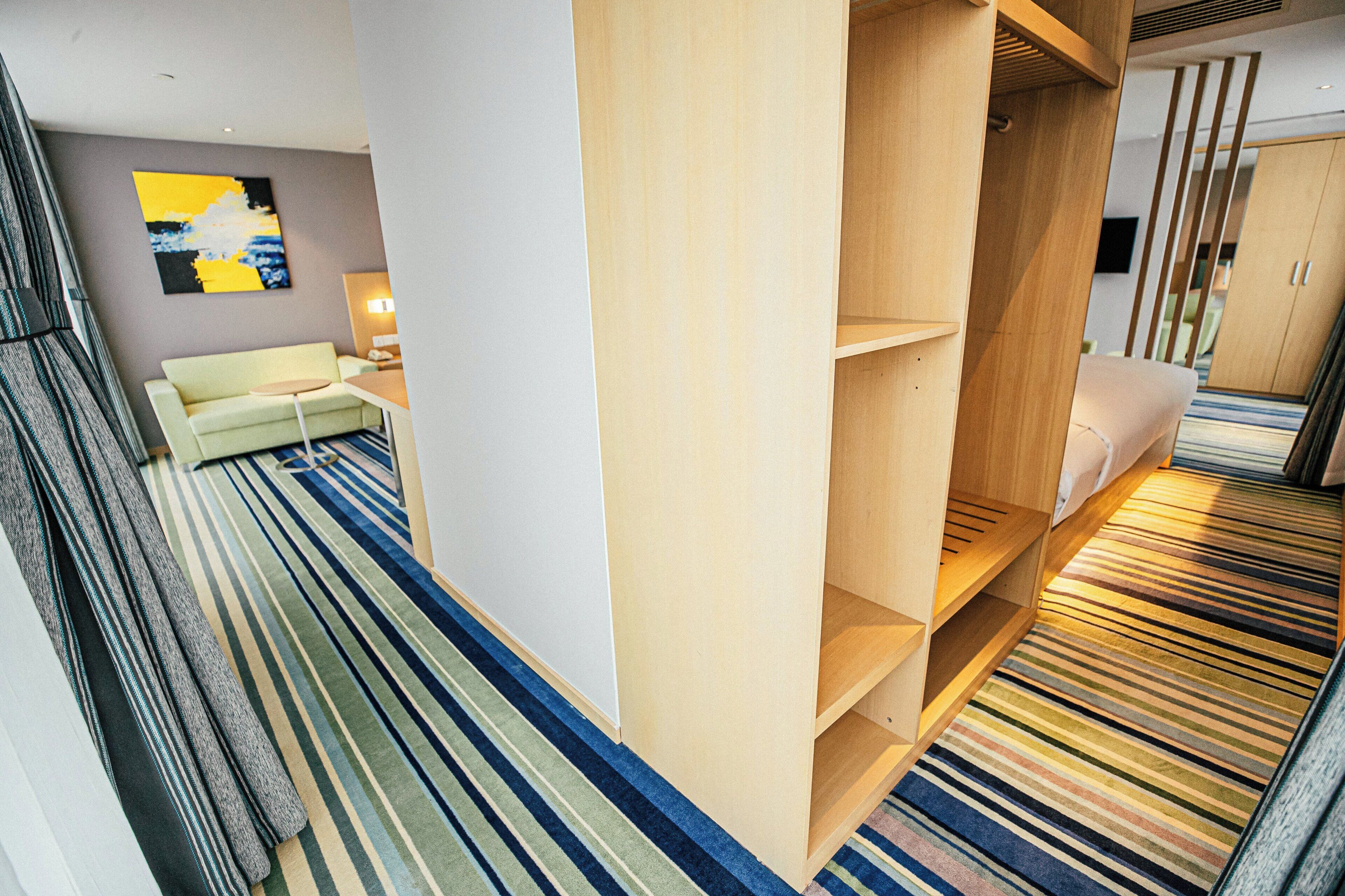 A hotel room with a sofa, a wooden wardrobe, and a striped carpet.