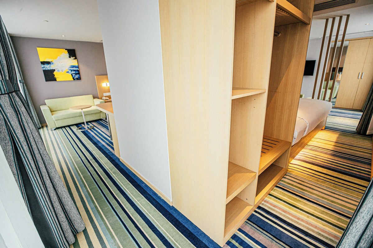 A modern hotel room with a sofa, a wooden wardrobe, and a striped carpet.