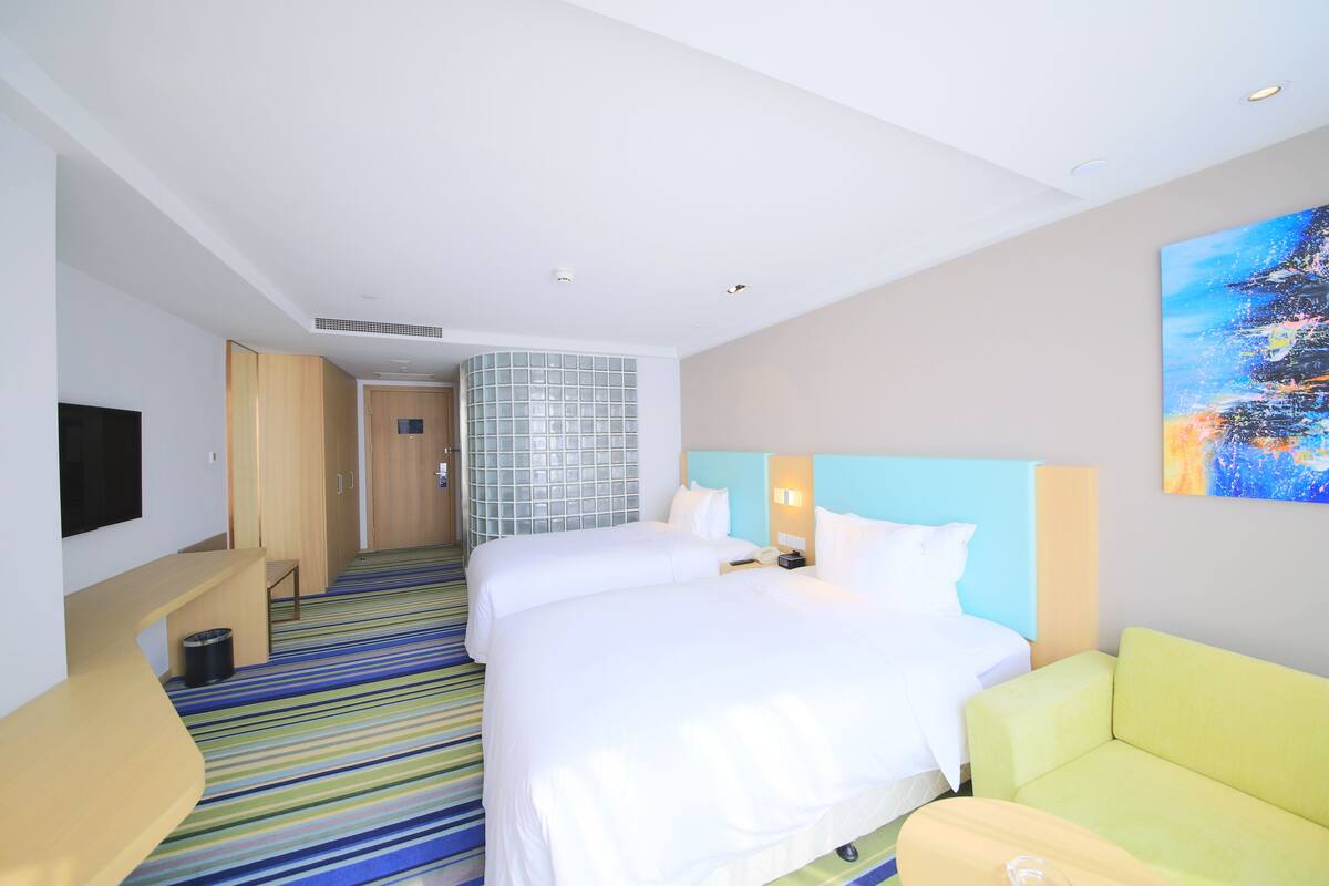 Habitación de hotel con dos camas, televisión, escritorio, sofá y una alfombra con rayas de colores.