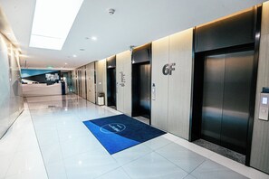 A modern hotel corridor with elevators, a reception area, and a blue mat with a logo. - Holiday Inn Express Yingkou Onelong Plaza by IHG (Yingkou)
