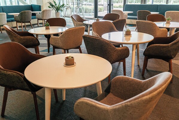 A modern lounge area with round tables and comfortable chairs, a blue sofa, and potted plants.
