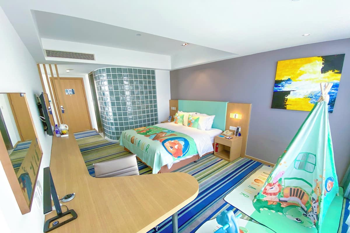 Habitación de hotel con cama, escritorio, silla, espejo, ventana y un cuadro en la pared.