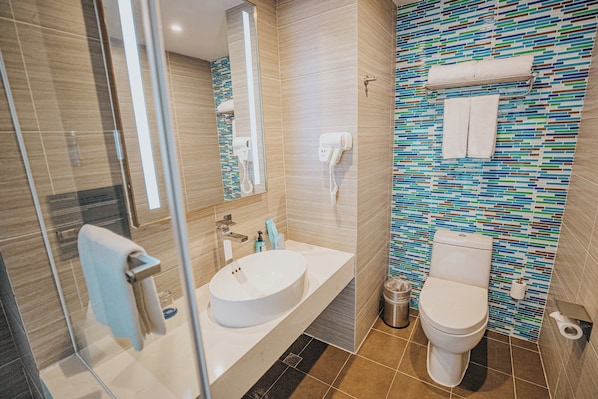 Un baño moderno con cabina de ducha de vidrio, un lavabo blanco y un inodoro.