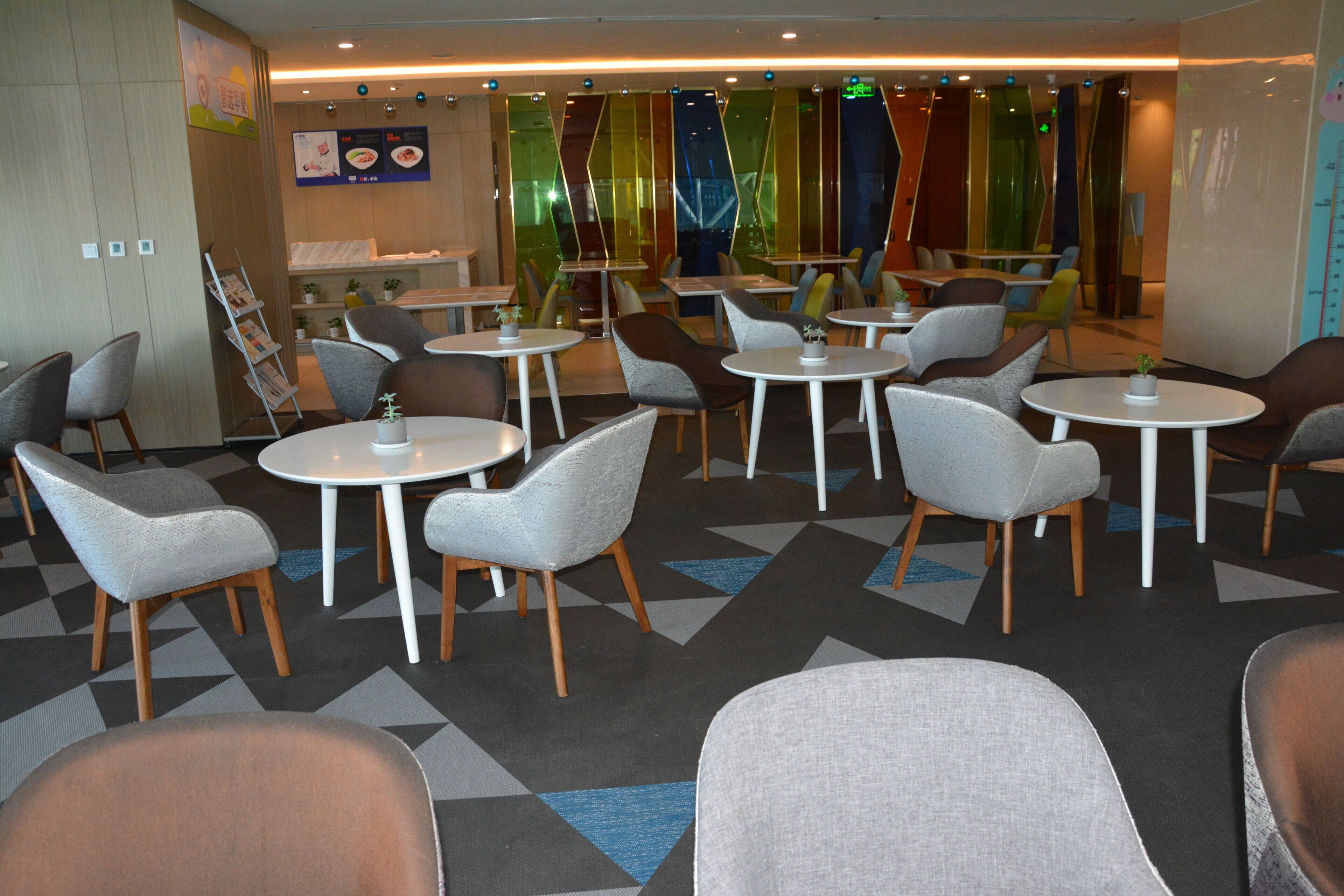 A modern dining area with round tables and chairs, a menu board, and a plant on the tables.