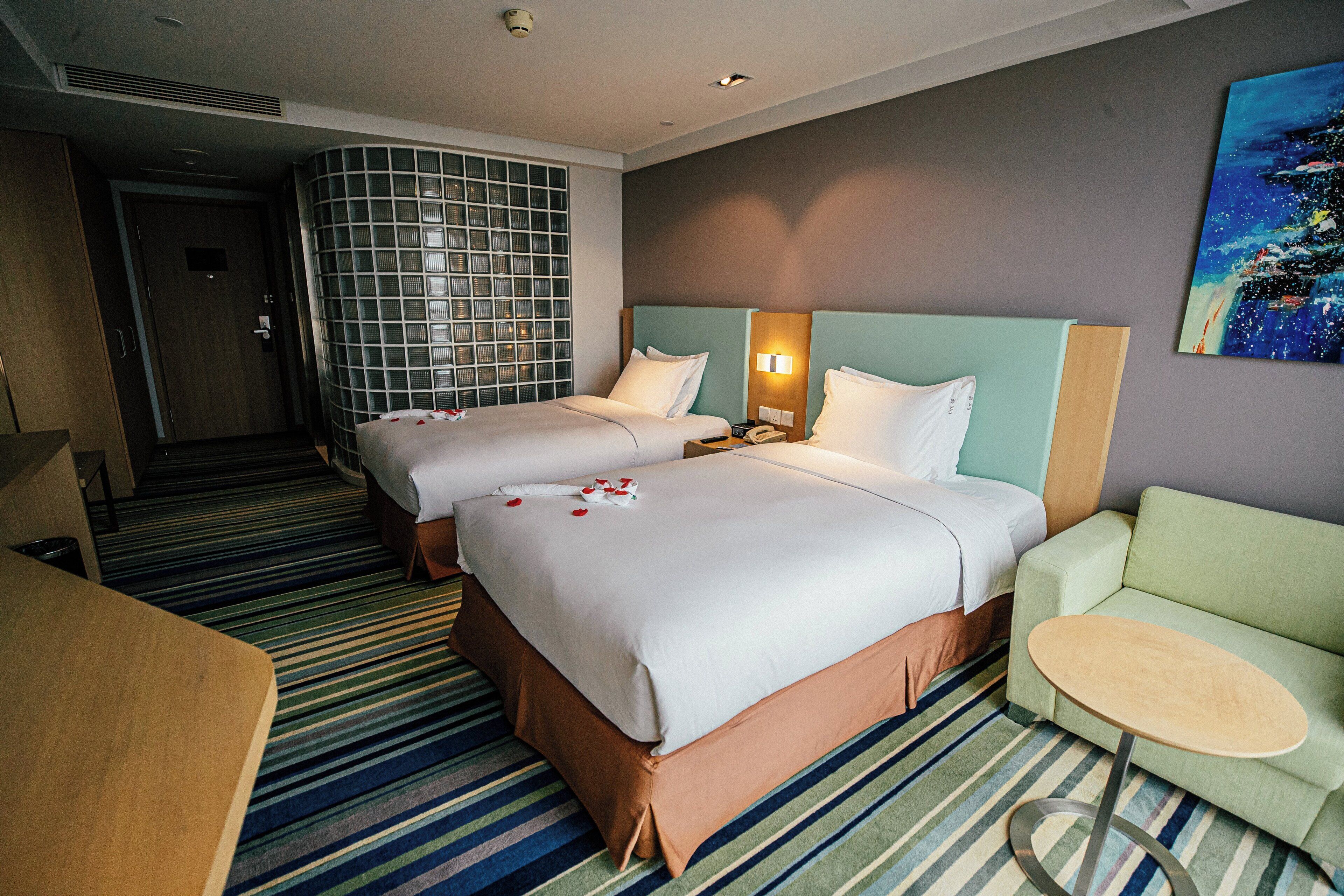 A hotel room with two beds, a sofa, a small table, and a painting on the wall.