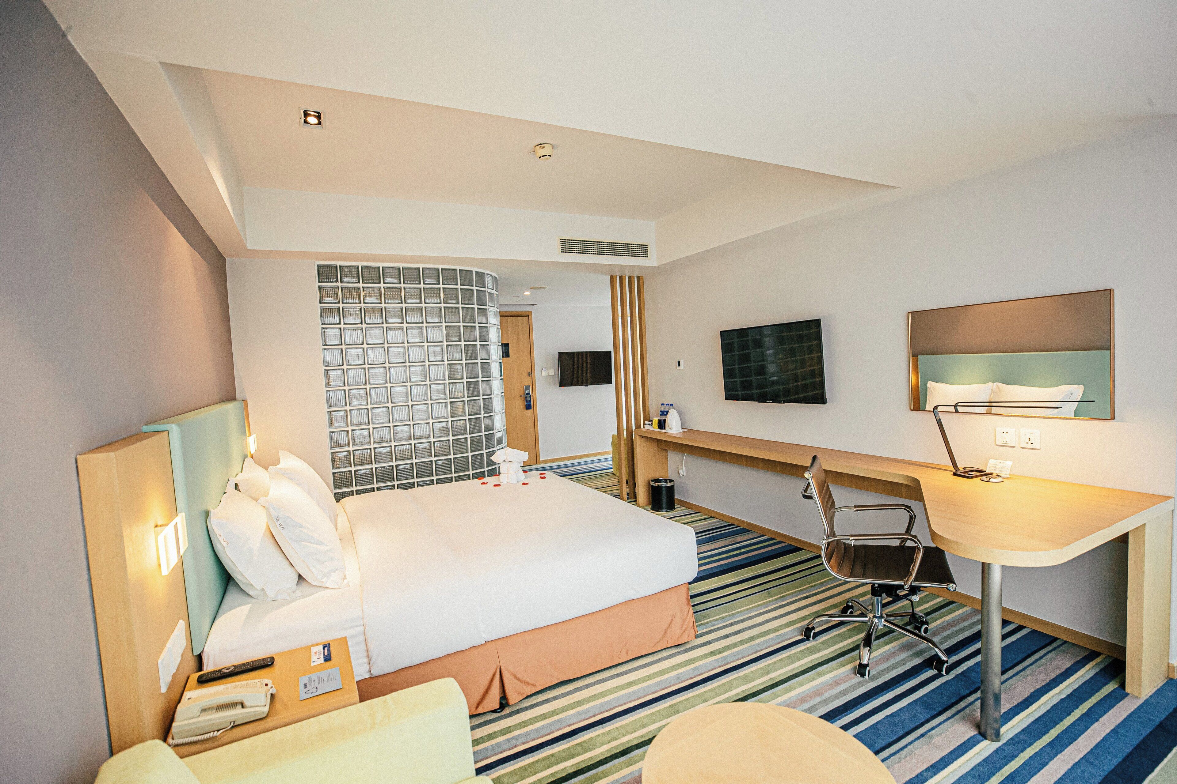 A hotel room with a bed, desk, chair, TV, and a striped carpet.