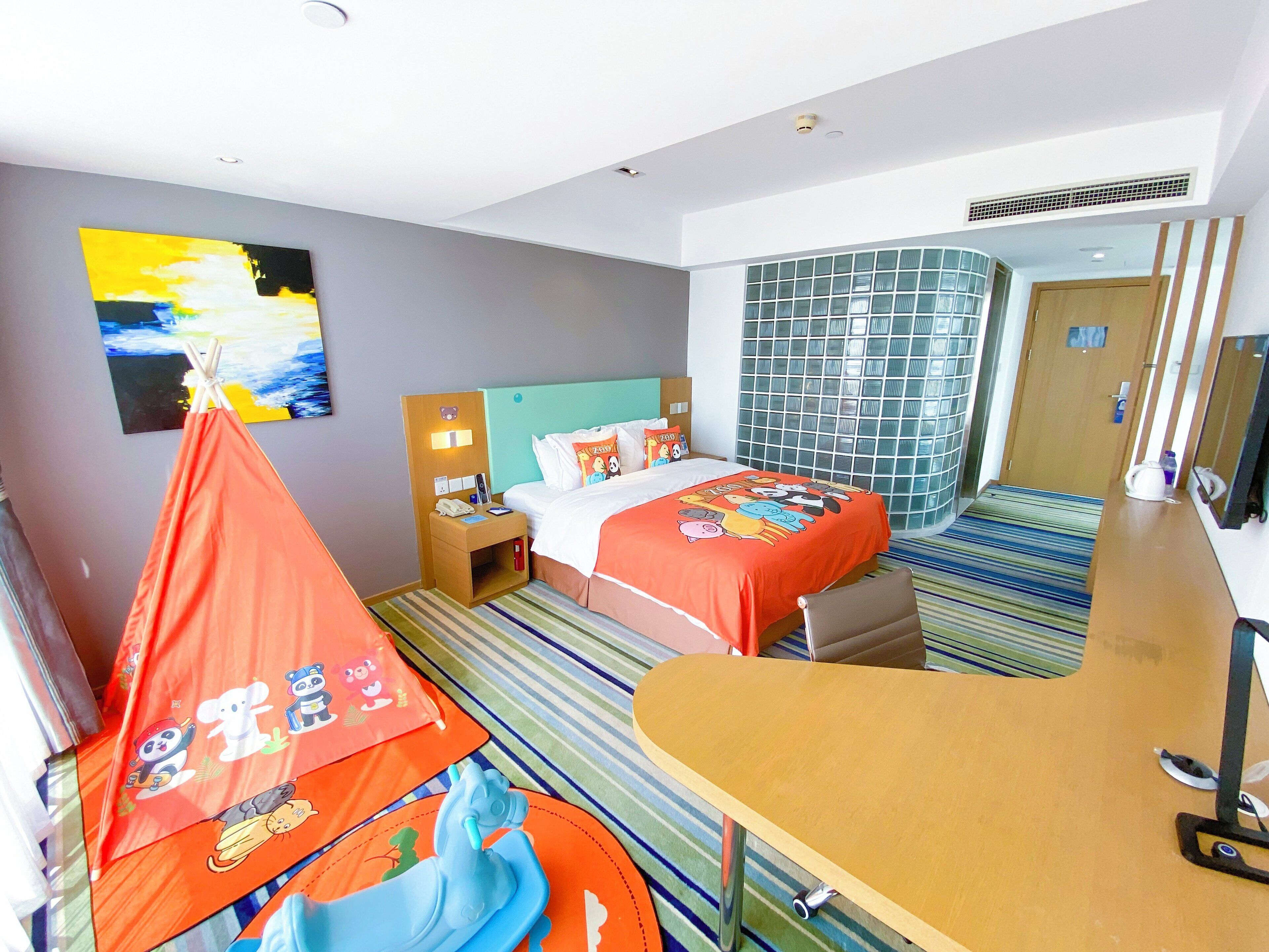 A hotel room with two beds, a desk, a chair, a hanging chair, a window with a view, and a painting on the wall.