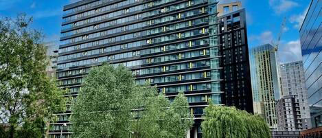 A modern multi-story hotel with a glass facade, located in an urban setting with trees and other buildings around.