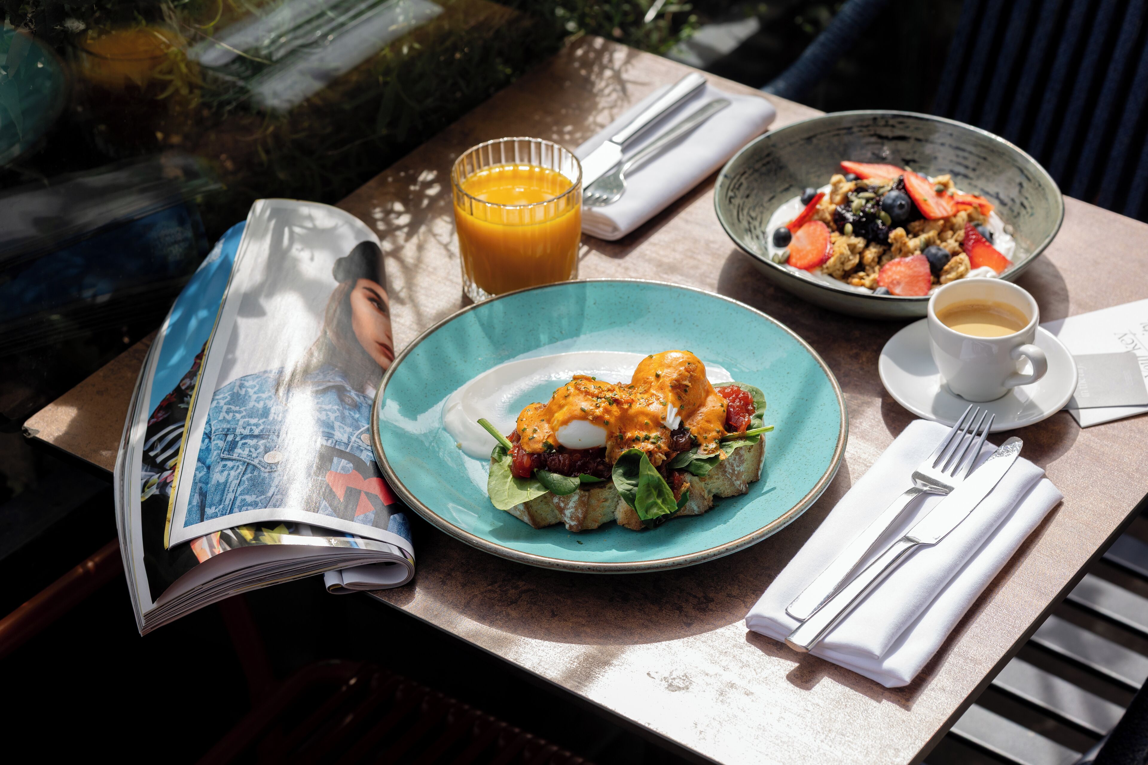 A table with a meal, a glass of orange juice, a cup of coffee, and a magazine.