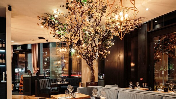 A restaurant interior with wooden tables, cushioned seating, and a large artificial tree centerpiece. - CitySuites Aparthotel (Salford)
