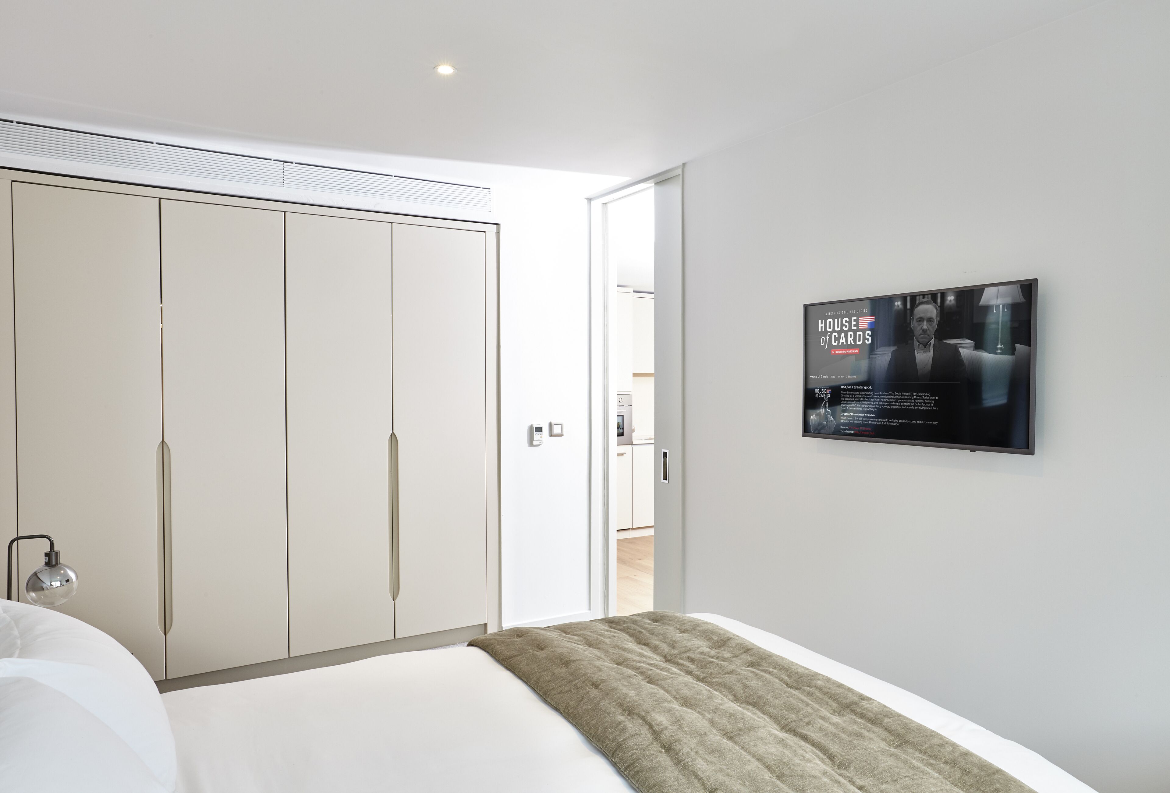 A modern bedroom with a bed, a wardrobe, and a television displaying 'House of Cards'.