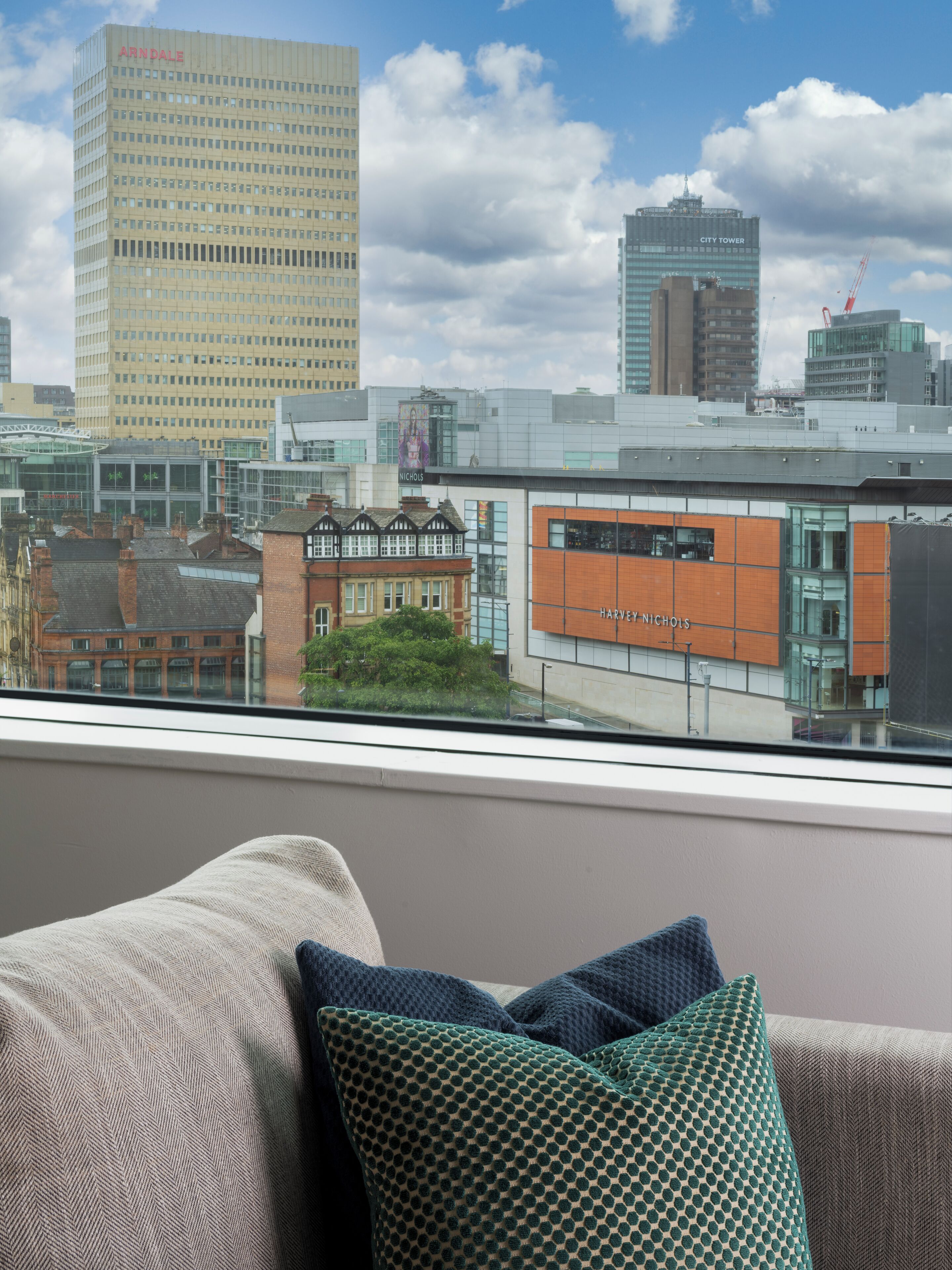 A city view from a window with a view of the Harvey Nichols store and the City Tower.