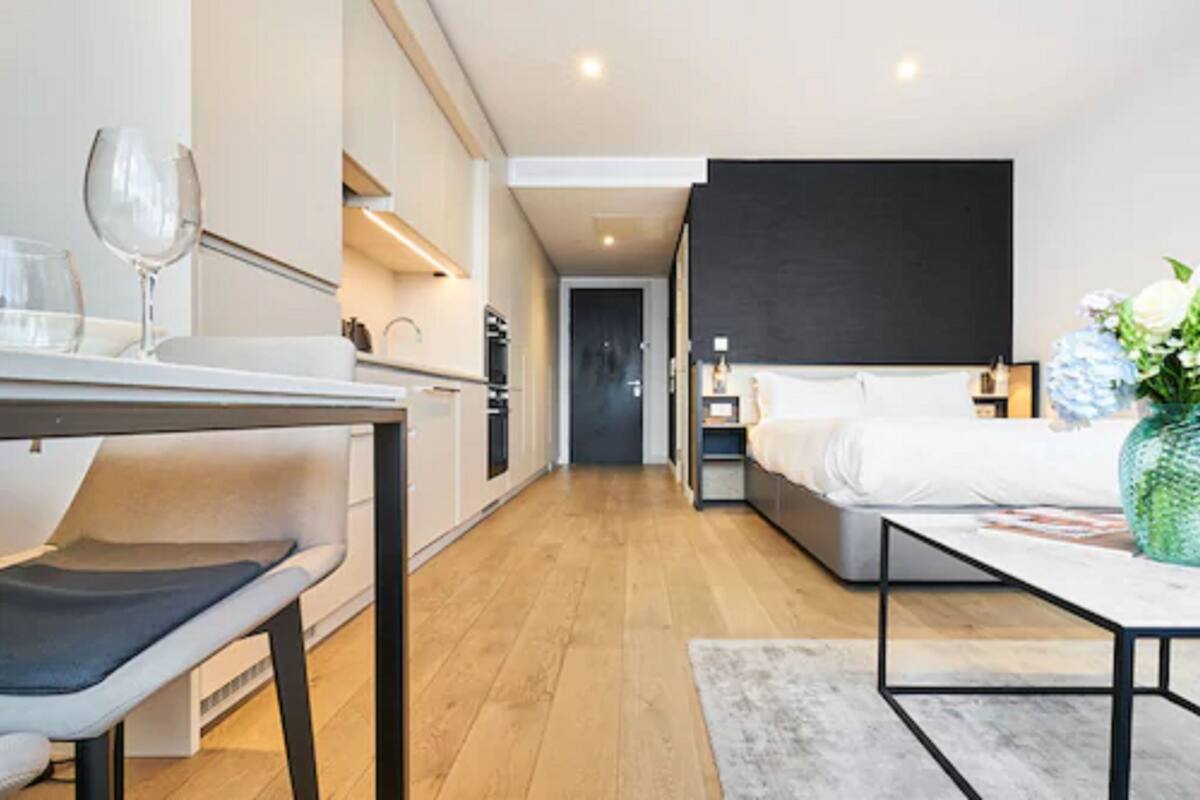 A modern hotel room with a bed, bedside table, and a small desk area with a chair.