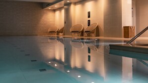 A swimming pool with a clear water surface, surrounded by walls with a brick pattern on one side and plain walls on the other. There are three chairs near the pool, and a wooden crate is visible in the corner. - CitySuites Aparthotel (Salford)