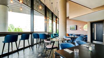 A modern restaurant with bar seating, large windows, and a view of greenery.