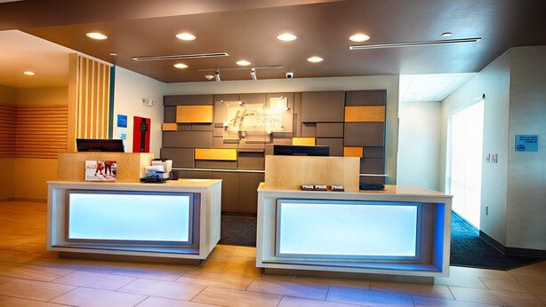 A hotel reception area with two reception desks, a modern design with recessed lighting, and a large mirror above the desks. - Holiday Inn Express & Suites Houston SW - Galleria Area by IHG (Houston)