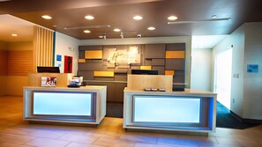 A hotel reception area with two reception desks, a modern design with recessed lighting, and a large mirror above the desks. - Holiday Inn Express & Suites Houston SW - Galleria Area by IHG (Houston)