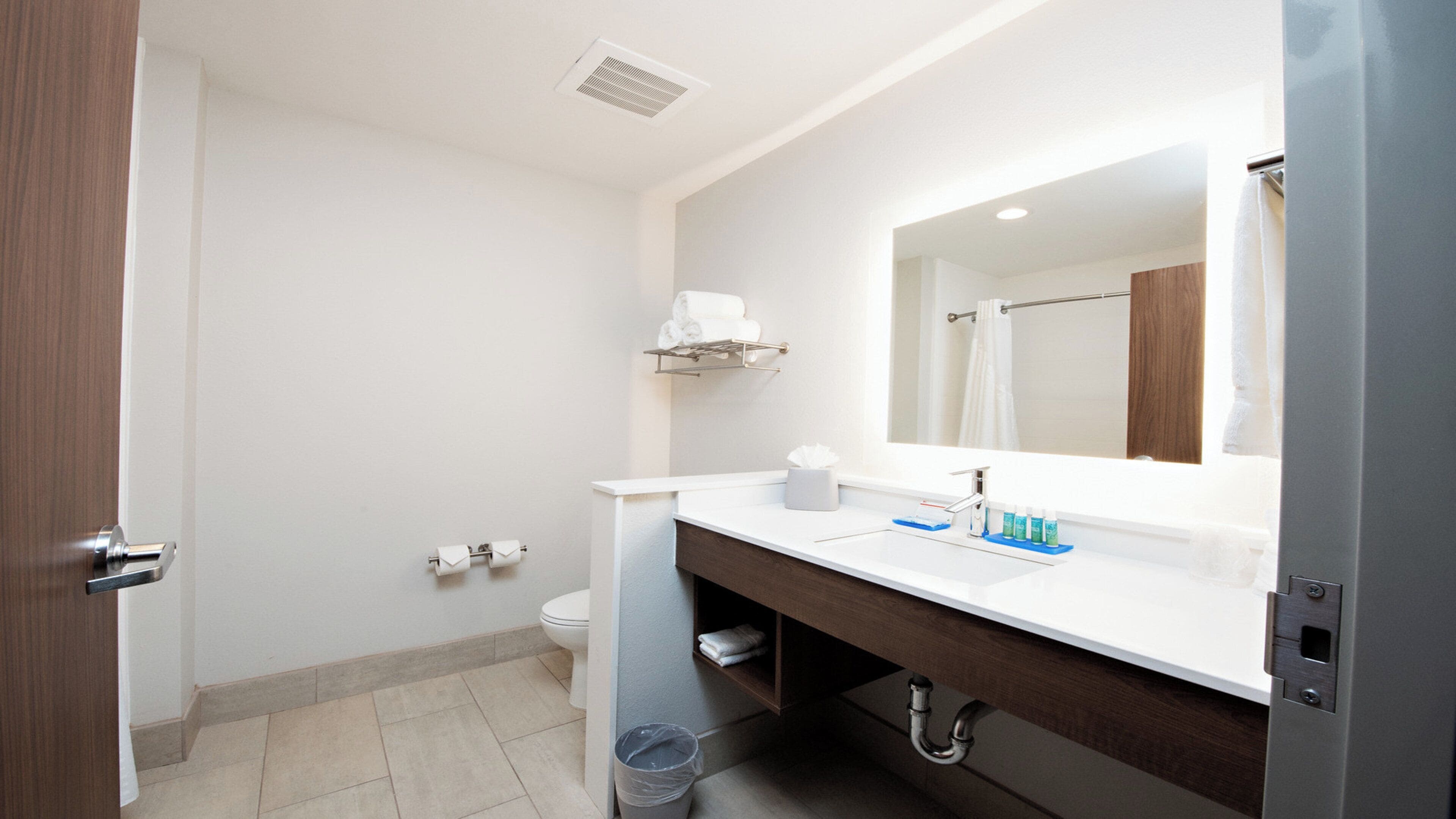 Un baño de hotel con un lavamanos blanco, un espejo, un perchero para toallas y un inodoro.