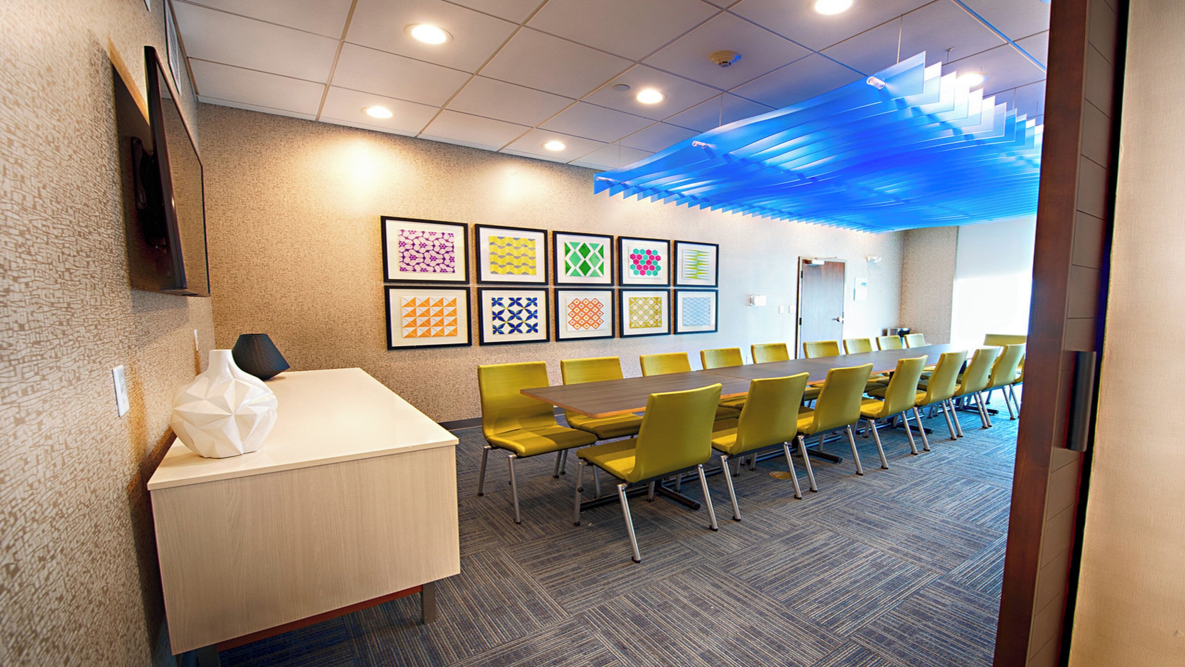 A conference room with a long table, yellow chairs, and framed artwork on the wall.
