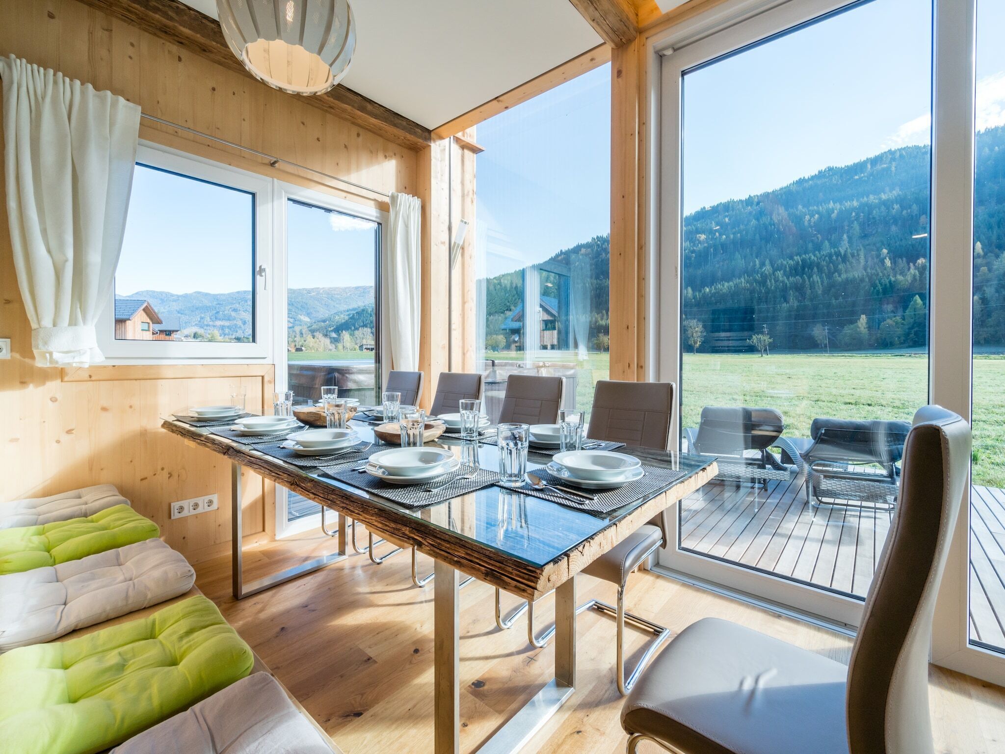 Un coin repas avec une table dressée pour quatre personnes, de grandes fenêtres et une vue sur un paysage montagneux.