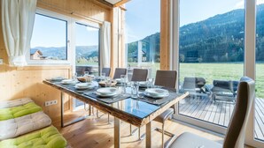 A dining area with a table set for four, large windows, and a view of a mountainous landscape. - Premium chalet with whirlpool (Murau)