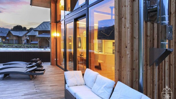 A modern building with large windows, a wooden deck with lounge chairs, and a view of the surrounding area. - Premium chalet with whirlpool (Murau)