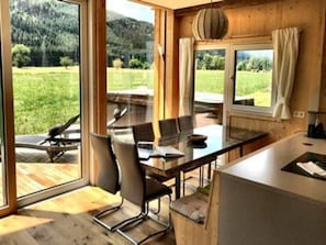 A modern kitchen with a large island, wooden flooring, and large windows offering a view of a green landscape. - Premium chalet with whirlpool (Murau)