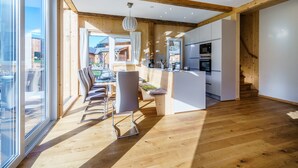 A modern kitchen with wooden beams, a dining area with a table and chairs, and large windows offering a view of the outside. - Premium chalet with whirlpool (Murau)