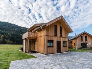 A wooden cabin with a balcony, a stone foundation, and a paved driveway. - Premium chalet with whirlpool (Murau)
