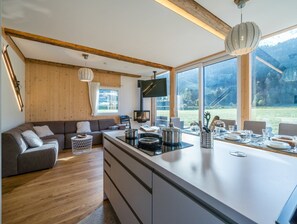 Uma cozinha moderna com uma ilha grande, vigas de madeira e grandes janelas que oferecem vista para o exterior.