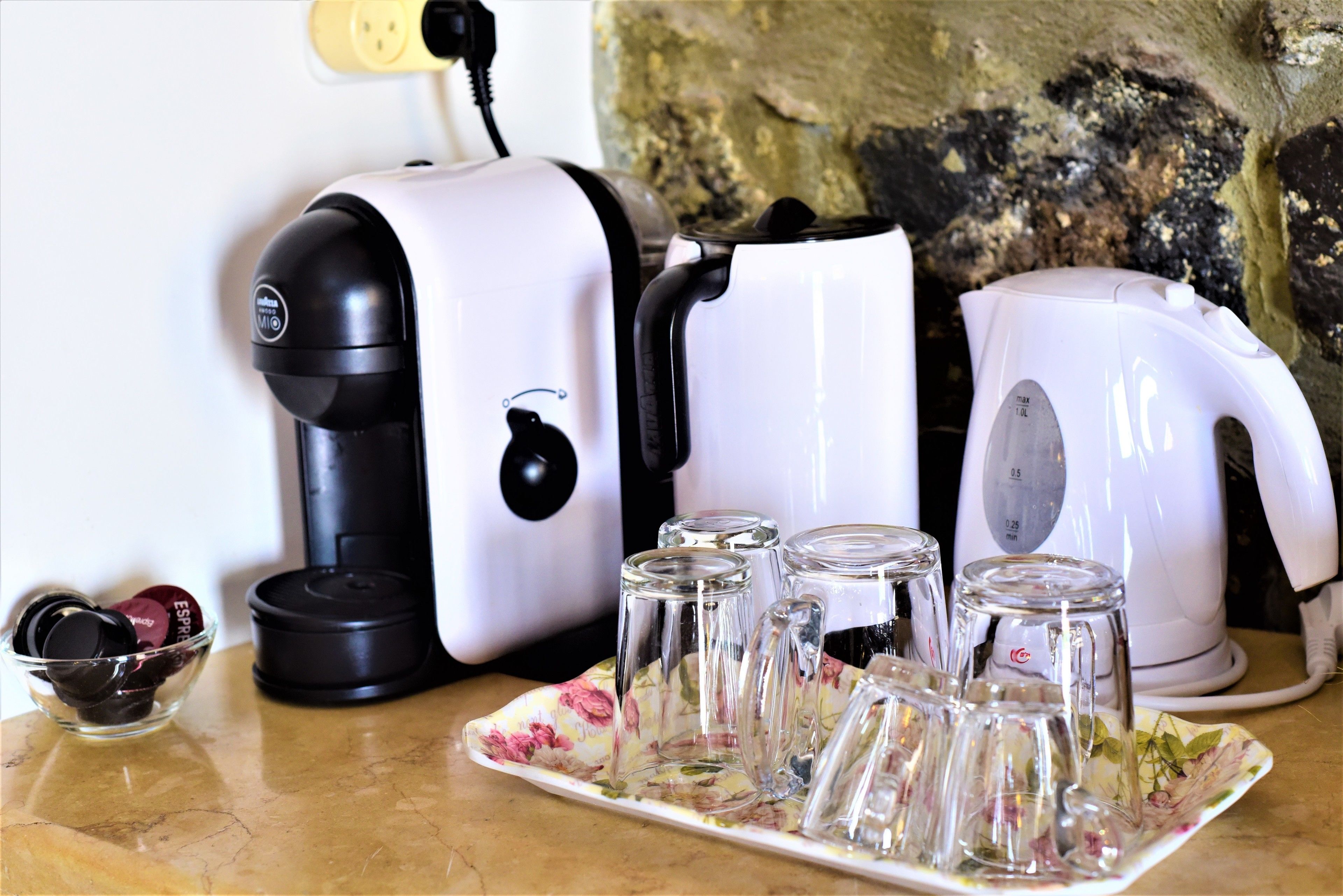 Eine Küchenarbeitsplatte mit Kaffeemaschine, Wasserkocher und einer Teller mit Blumenmuster und Gläsern.