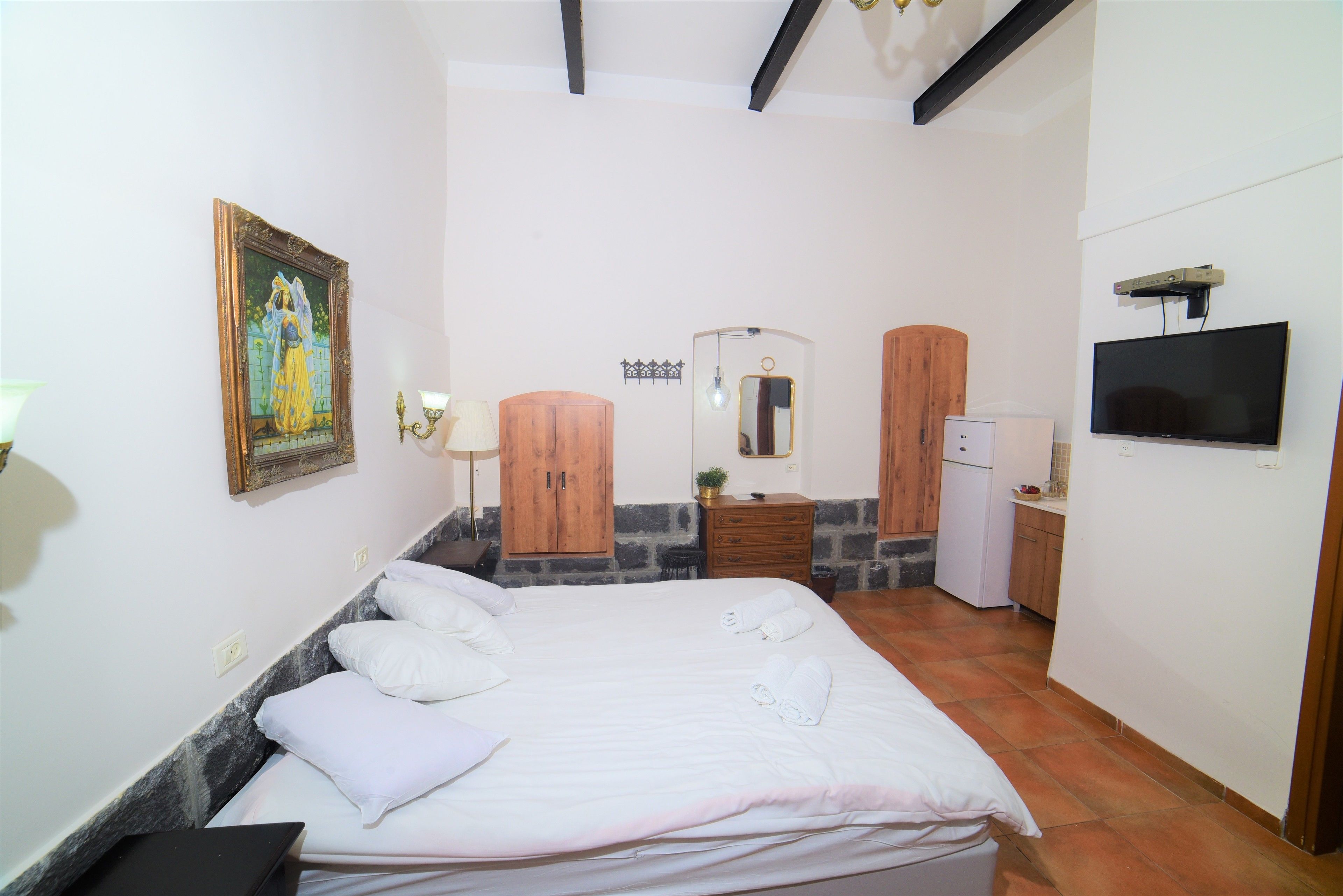 A hotel room with a bed, a dresser, a mirror, a television, and a painting on the wall.