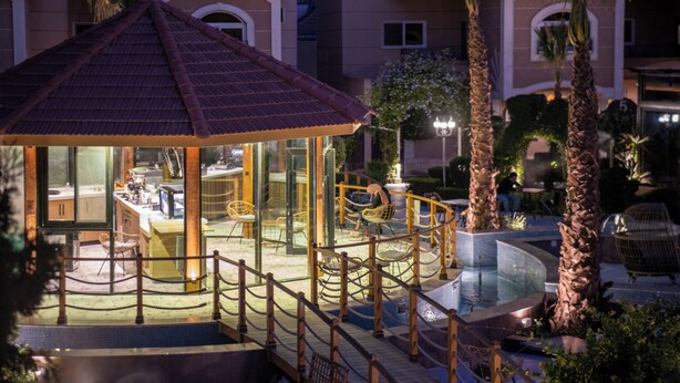 Un kiosque doté d’un toit en tuiles, entouré de palmiers et bordant une piscine.