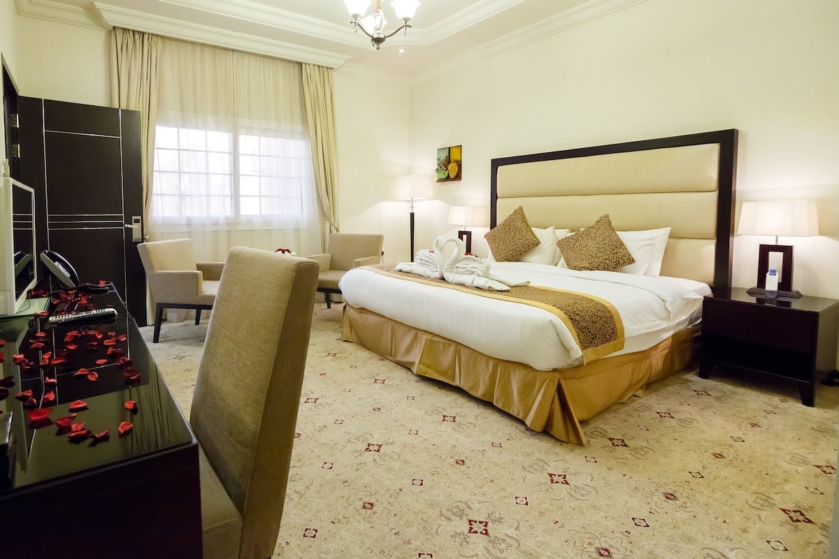 A hotel room with a large bed, a desk with a computer and a telephone, a chair, and a television.