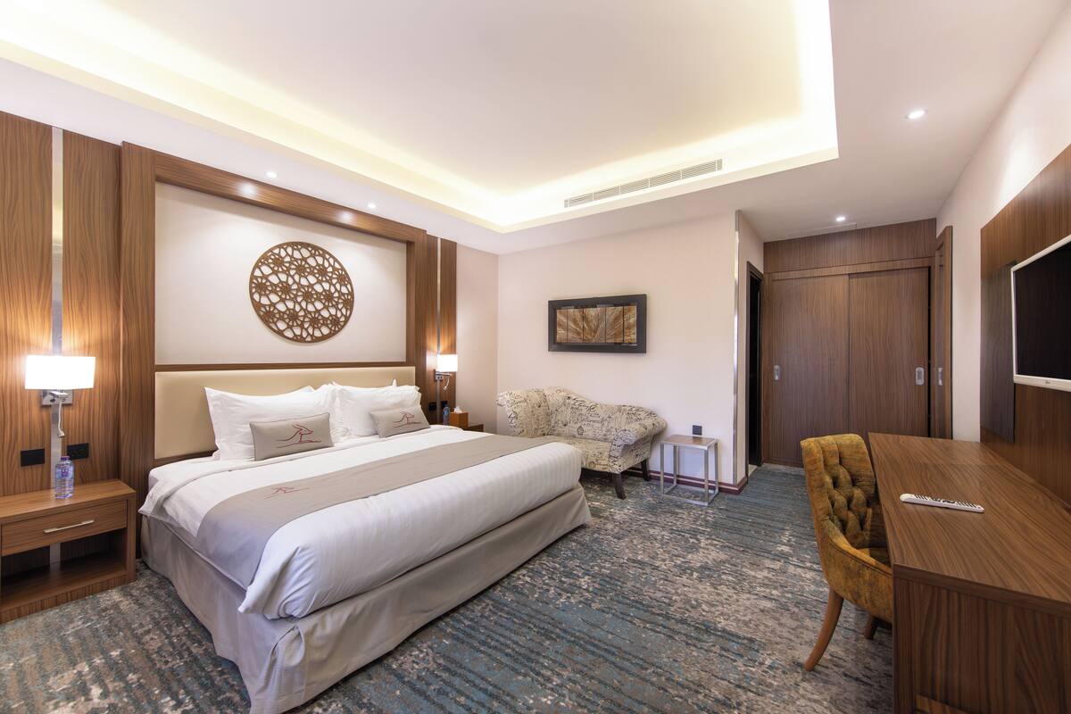 A hotel room with a large bed, a desk, a chair, a TV, and a wall with a circular design.